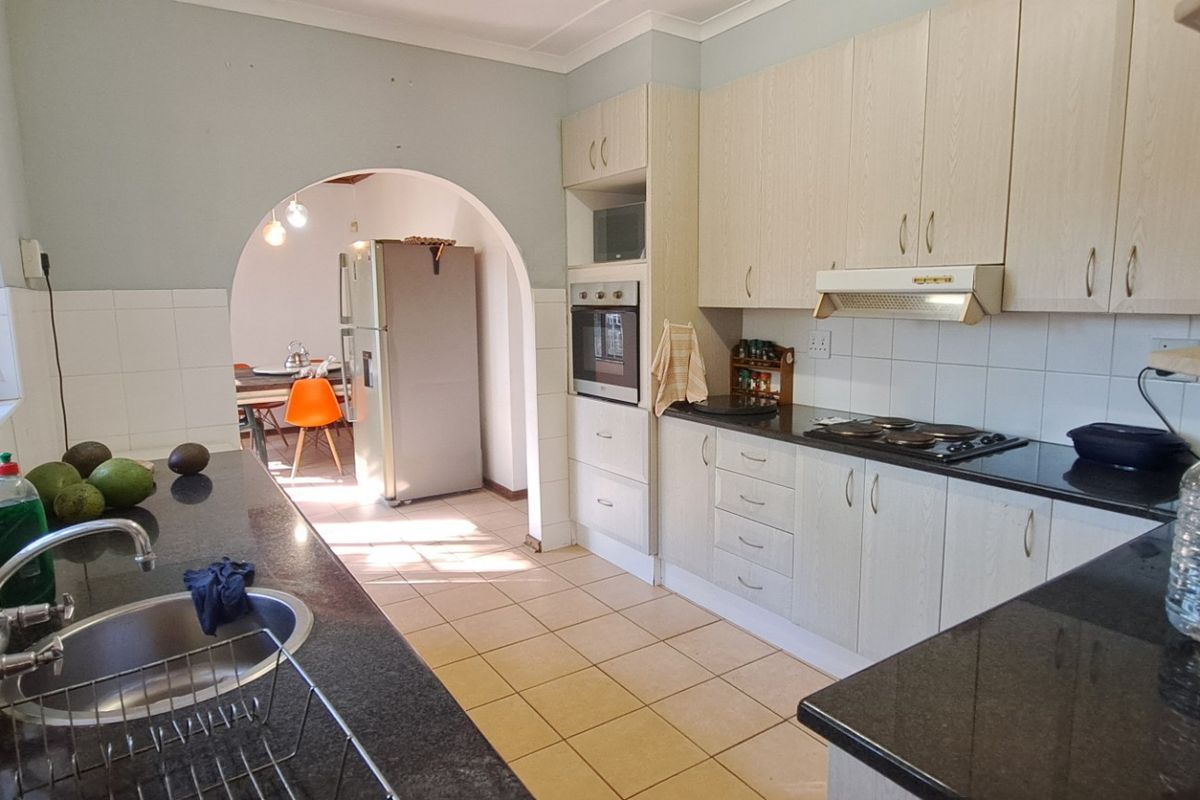A functional kitchen featuring light-toned cabinetry, granite countertops, built-in oven, and a tiled backsplash, leading through an archway to the dining area.