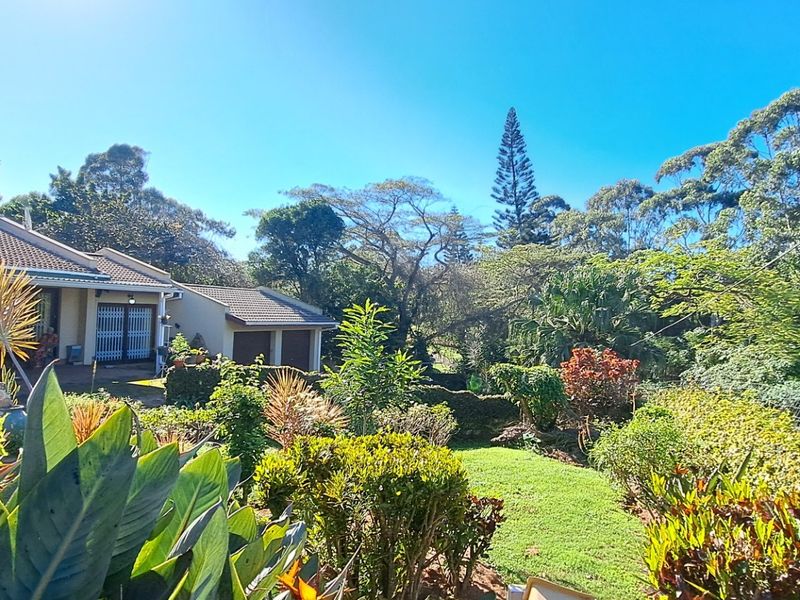 A view of the rear exterior of the house featuring a well-maintained garden, paved patio area, and double garage under a tiled roof.