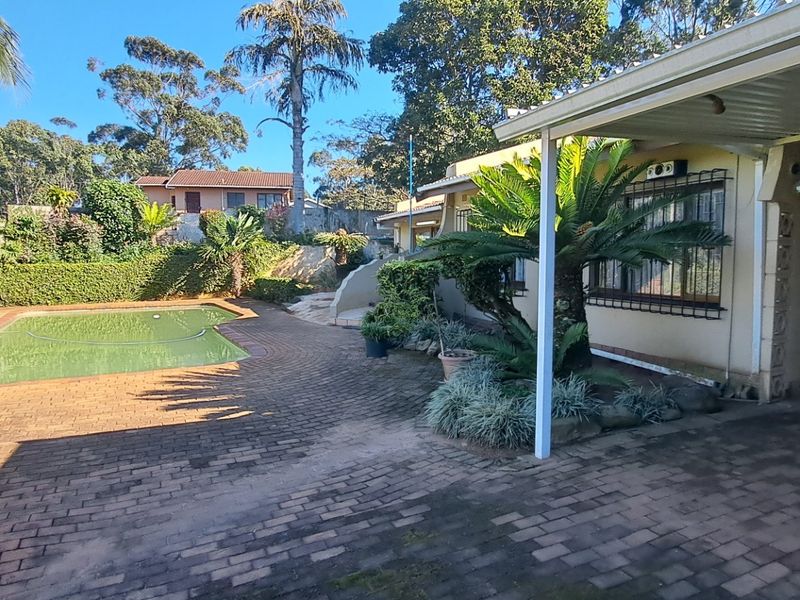 Rear exterior view featuring a paved patio area, covered veranda, and a swimming pool set within a landscaped garden.