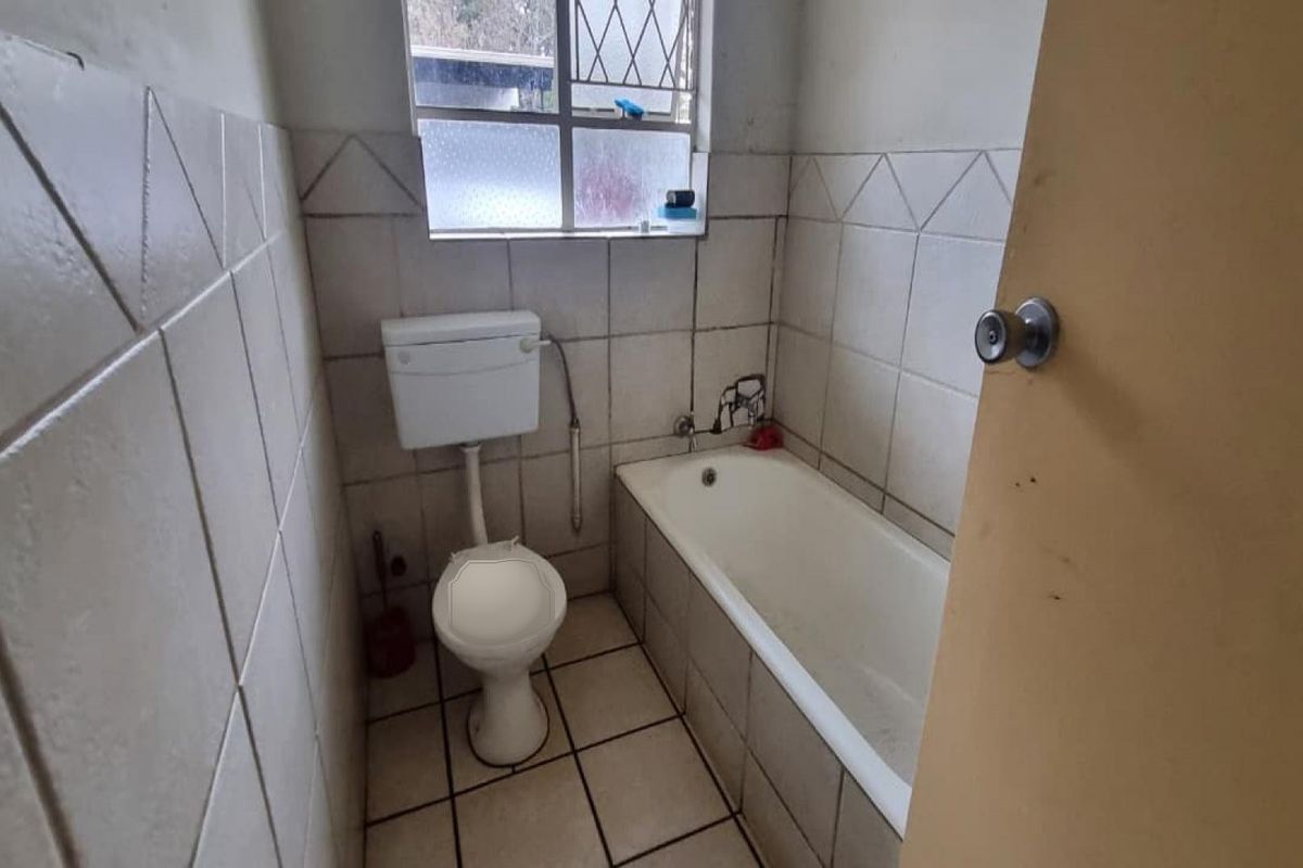 A compact bathroom featuring a standard bathtub, toilet, and tiled walls. The space is dated and requires cosmetic updates to improve its condition.