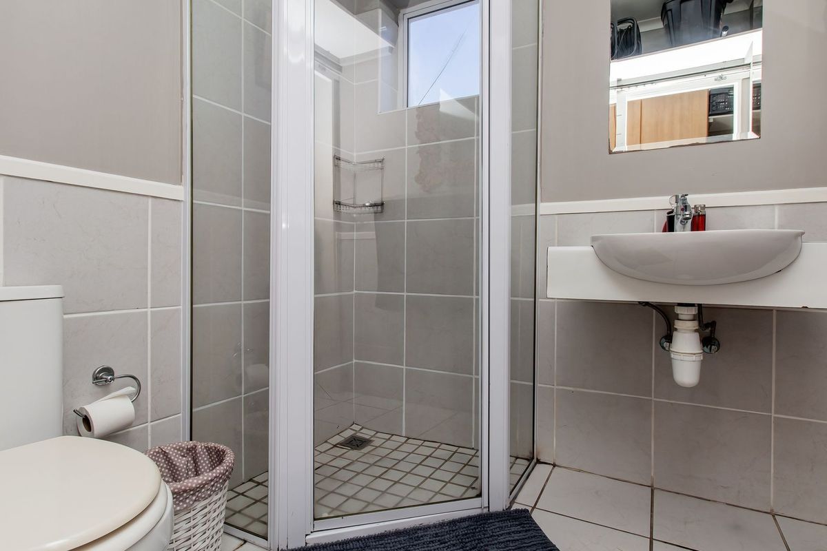 A compact bathroom featuring a glass-enclosed shower, wall-mounted basin, and toilet with neutral wall and floor tiling.