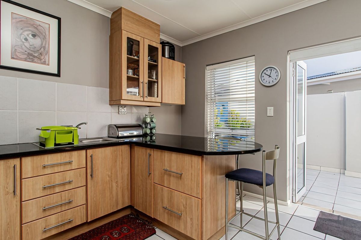 A functional kitchen featuring light wood cabinetry, black countertops, tiled backsplash, and direct access to an outdoor patio area.