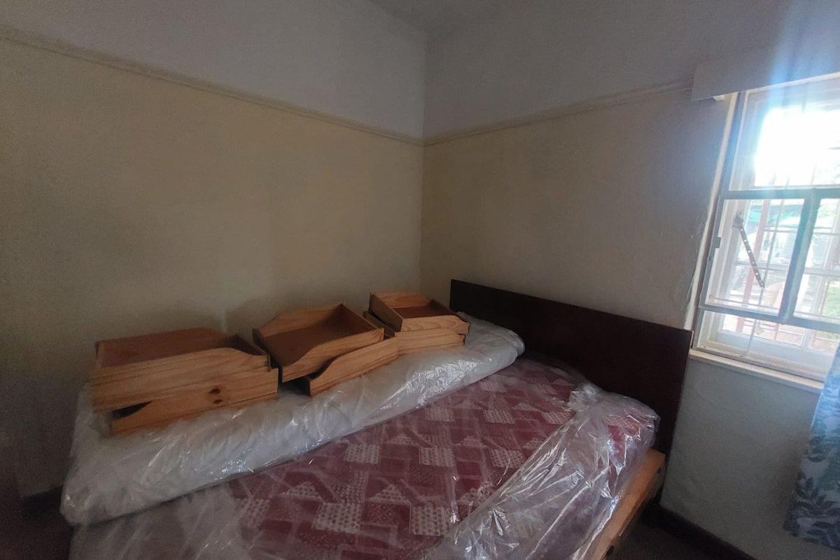 A bedroom featuring a window with security bars and traditional picture rails, requiring cosmetic updates to the wall finishes.