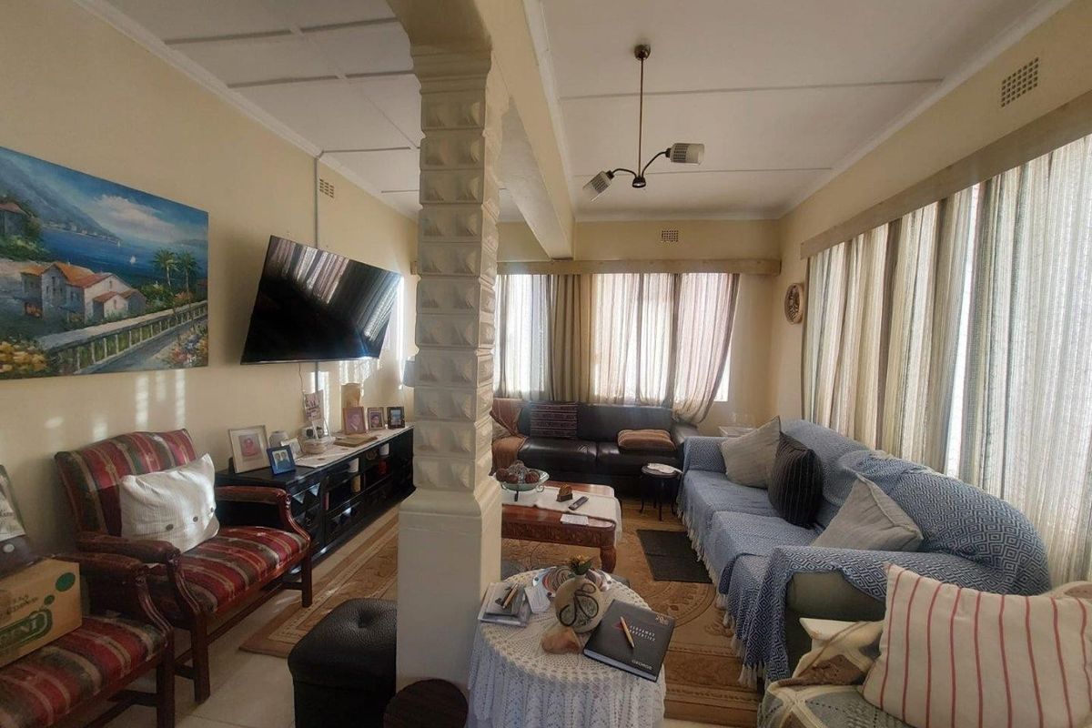 A living room featuring a central decorative pillar, tiled flooring, and large windows allowing for natural light.