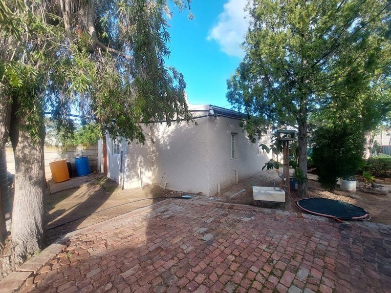 Rear view of the property featuring a brick-paved patio area, mature trees, and exterior wall access.