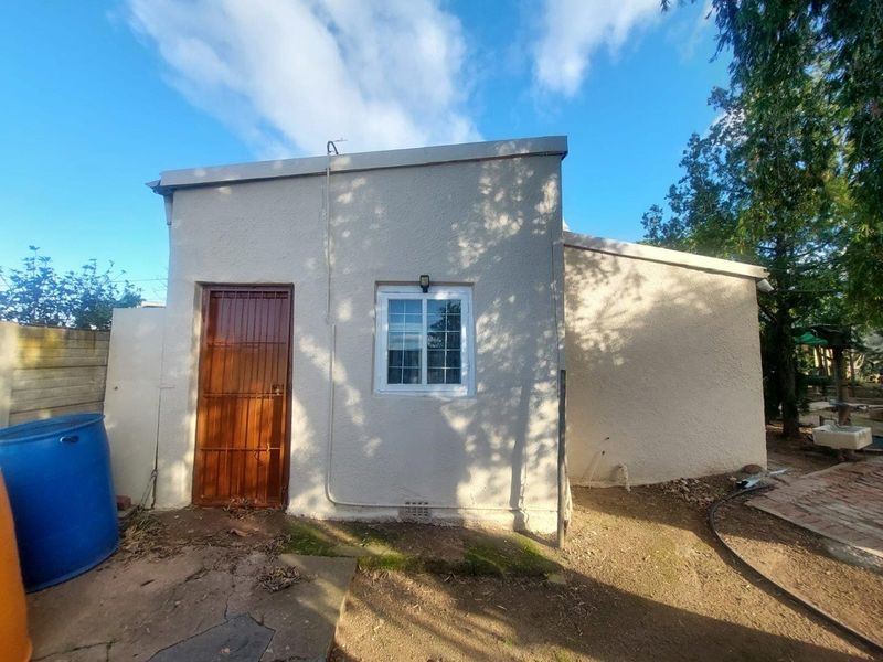 Rear exterior view of the property featuring a single door with security gate, a window, and surrounding outdoor space.