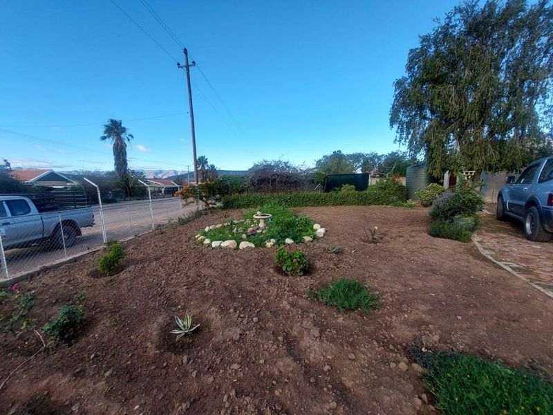 A view of the property's front garden area featuring a rock-bordered garden bed, established trees, and perimeter fencing.