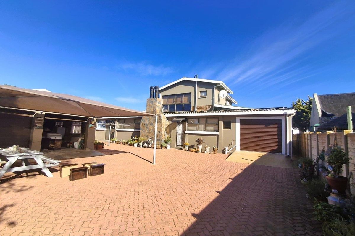 Rear exterior view of the property featuring a paved courtyard, covered patio area, stone-clad chimney, and a single garage with a roller door.