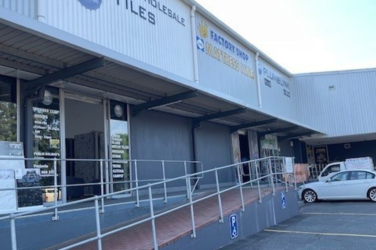 Exterior view of a commercial office and retail complex featuring a paved accessibility ramp with metal railings and multiple storefront entrances.