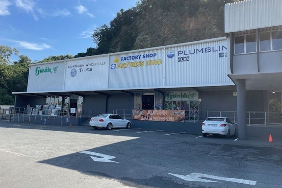 Exterior view of a commercial office and retail complex featuring multiple storefronts, paved parking area, and metal cladding facade.