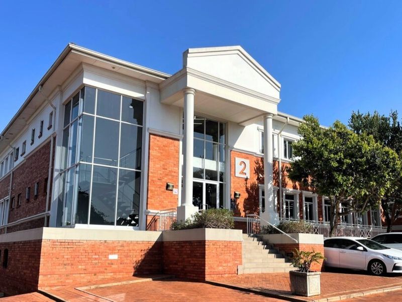 A professional office building exterior featuring a brick facade, large glass curtain walls, and a prominent columned entrance portico.