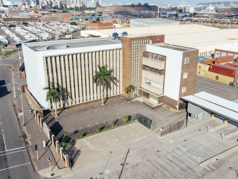 Aerial view of a multi-story office building featuring a paved parking area, security gatehouse, and perimeter fencing in an industrial urban setting.