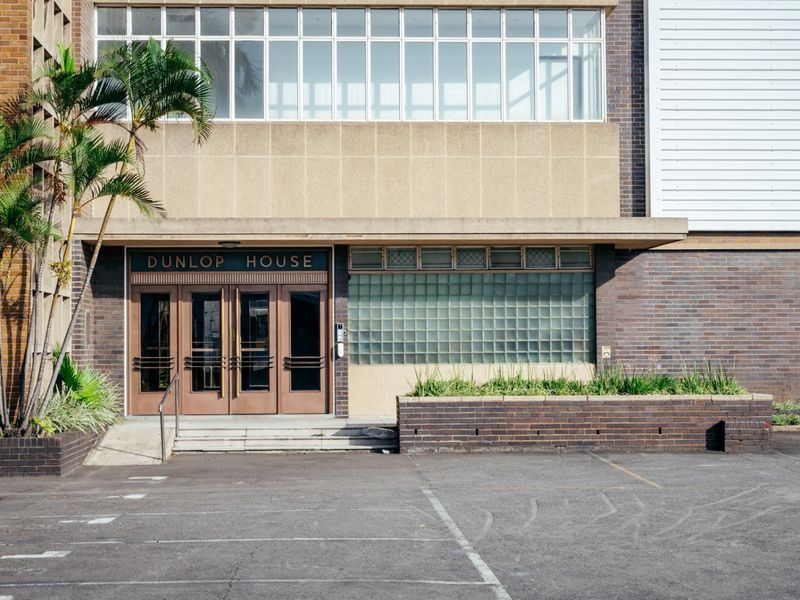 The main entrance of Dunlop House, featuring a classic brick facade, glass block detailing, and a paved parking area.