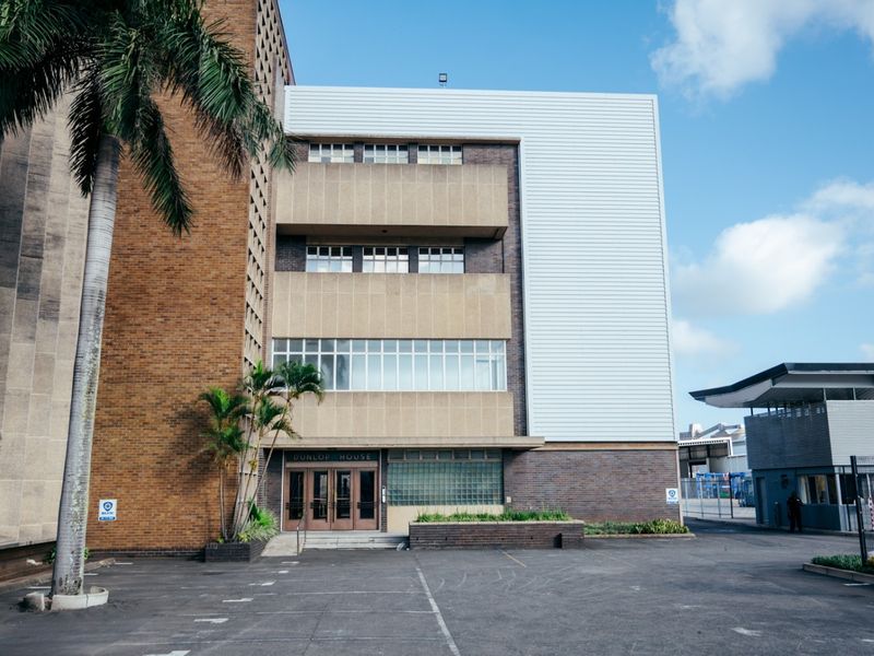 Exterior view of a multi-story office building featuring a brick and metal facade with a paved parking area and main entrance.