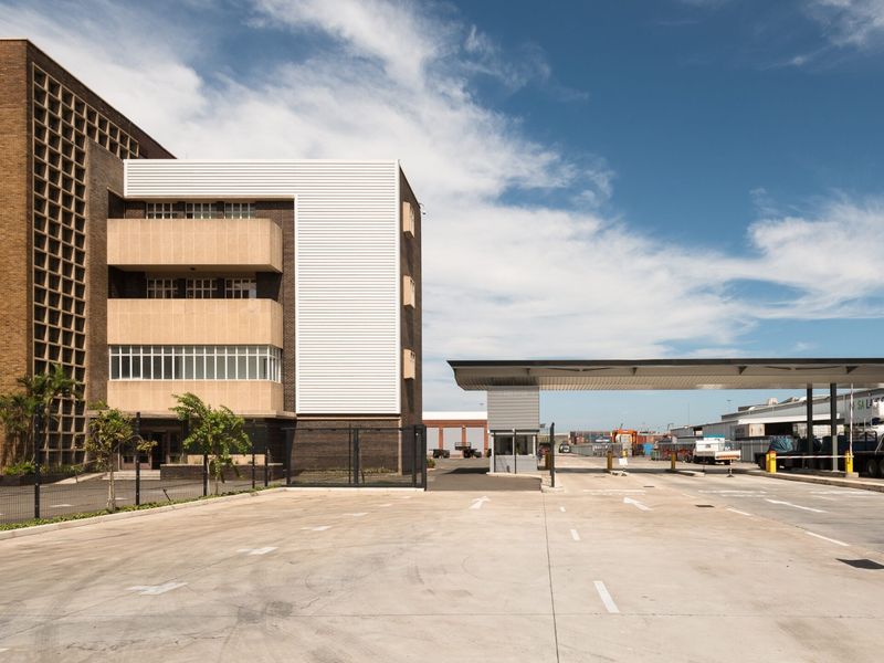 Exterior view of a commercial office building featuring a paved entrance, security gatehouse, and large canopy structure for vehicle access.