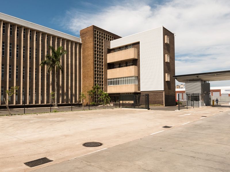 A professional exterior view of a multi-story office building featuring a paved parking area, security gatehouse, and modern architectural facade.