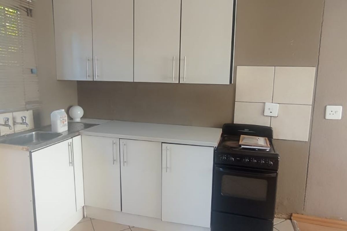 A compact kitchen featuring white cabinetry, a stainless steel sink, and a freestanding stove, requiring cosmetic updates to improve its overall appeal.