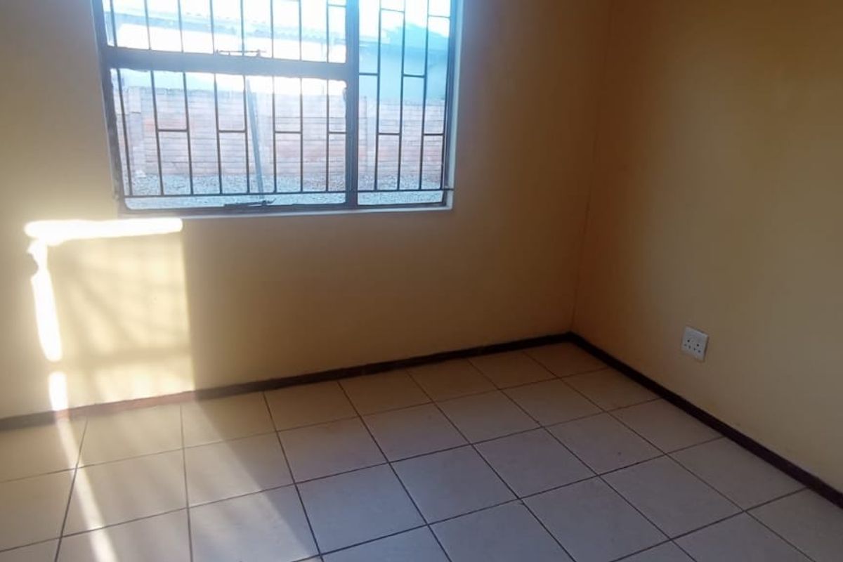 A vacant bedroom featuring tiled flooring, a window with security bars, and neutral wall finishes.