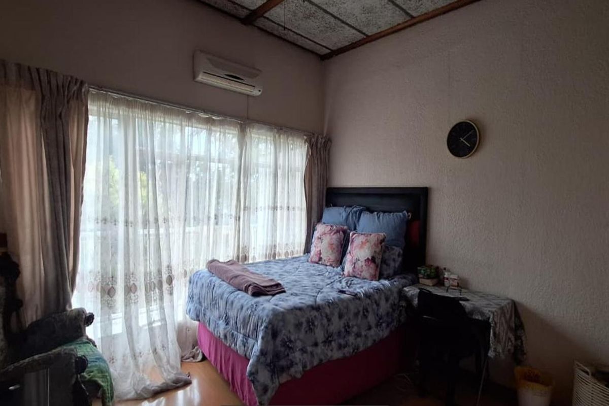 A bedroom featuring a wall-mounted air conditioning unit, large window with curtains, and textured ceiling finish.