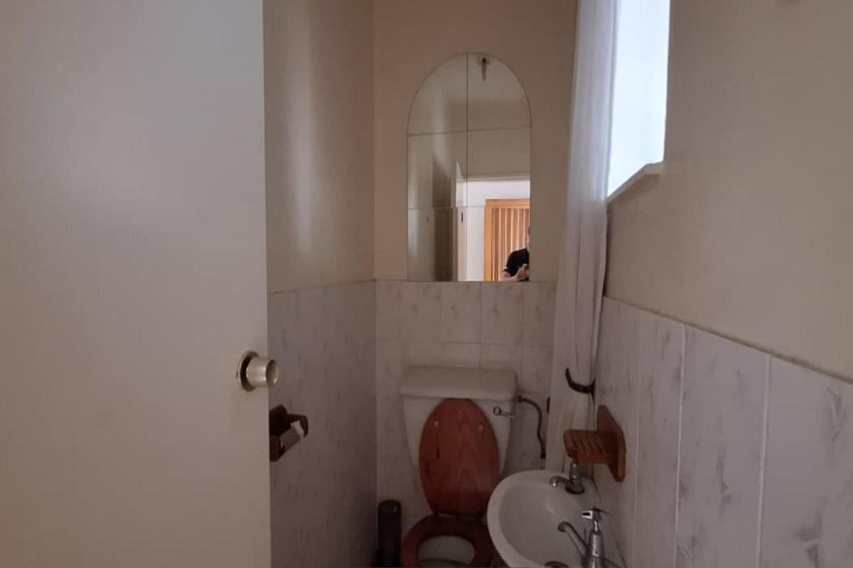 A compact guest bathroom featuring a wall-mounted basin, toilet, and arched mirror with partial wall tiling.