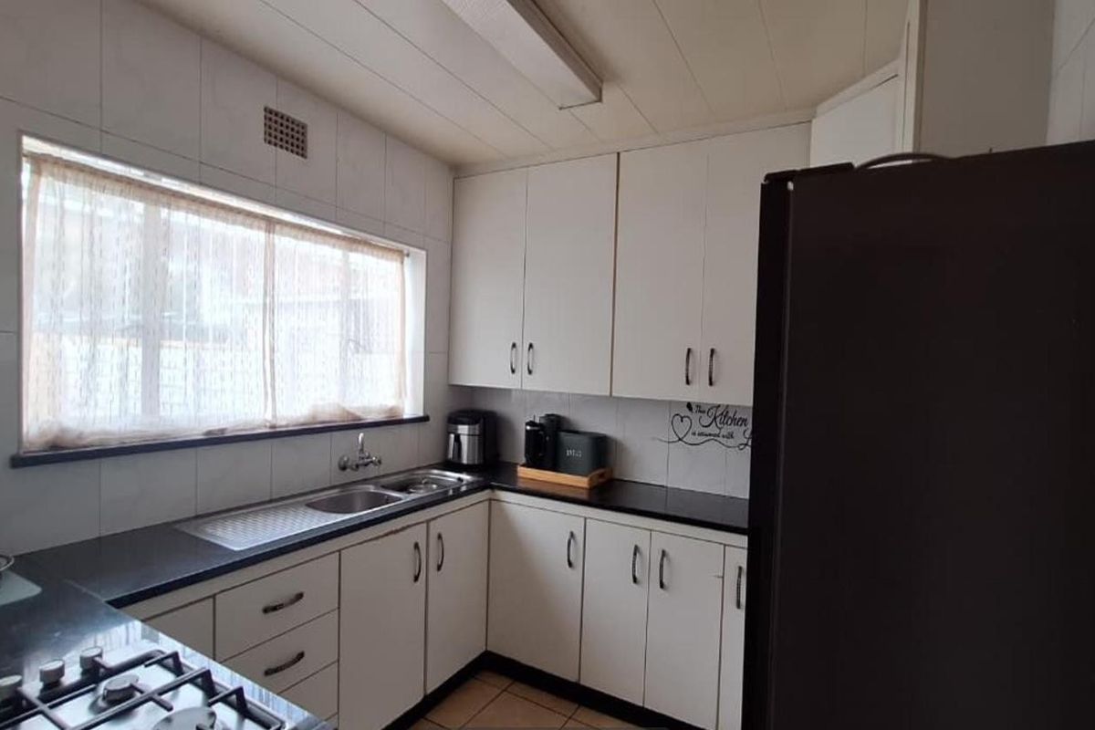 A functional kitchen featuring white cabinetry, dark countertops, a stainless steel sink, and a built-in gas hob, offering a clean and practical workspace.