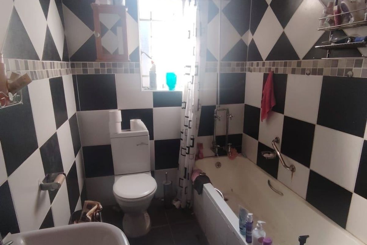 A functional bathroom featuring a bathtub with shower attachment, toilet, and pedestal basin, finished with high-contrast black and white checkered wall tiling.