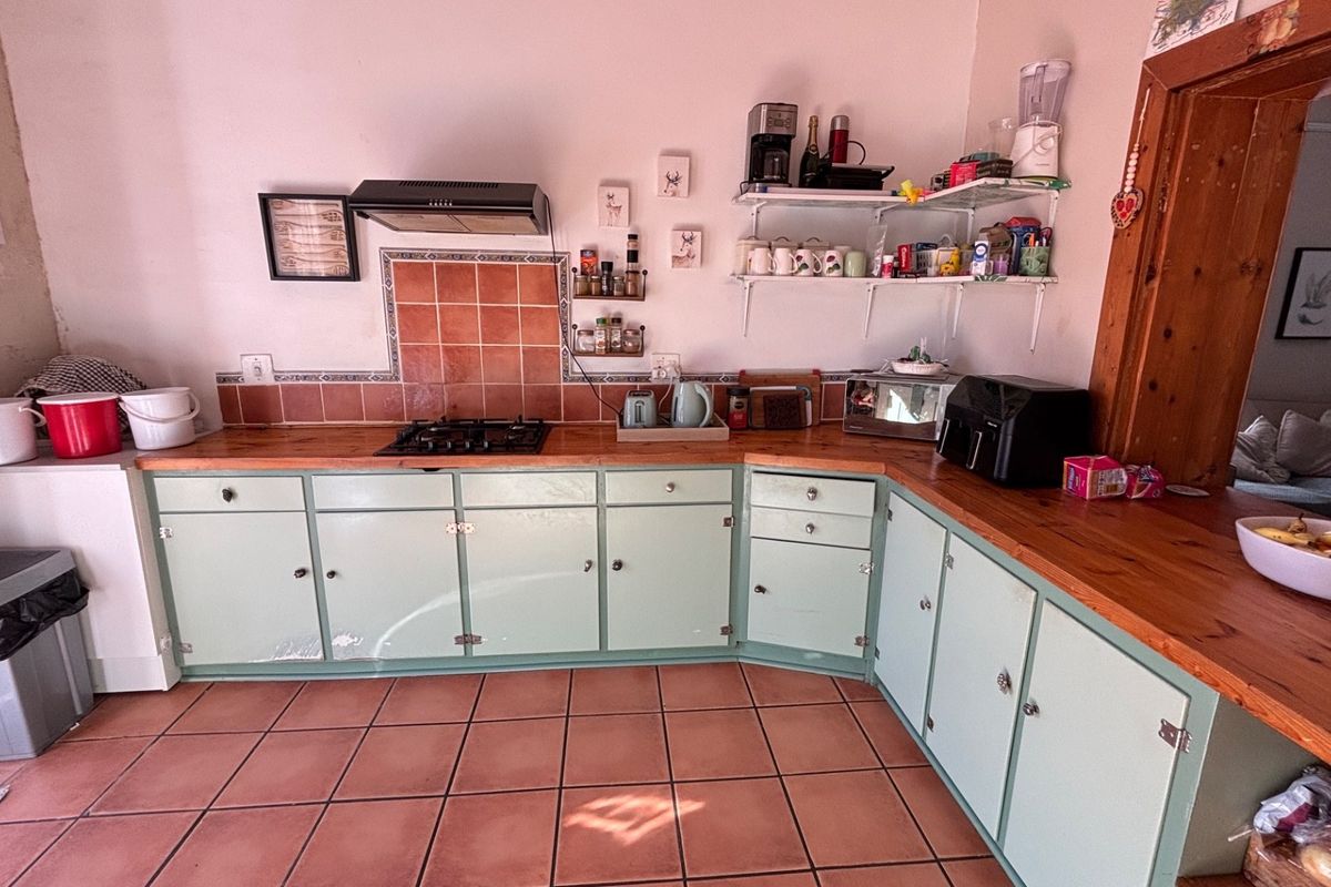A functional kitchen featuring light green cabinetry, wooden countertops, a gas hob with extractor fan, and terracotta floor tiles.
