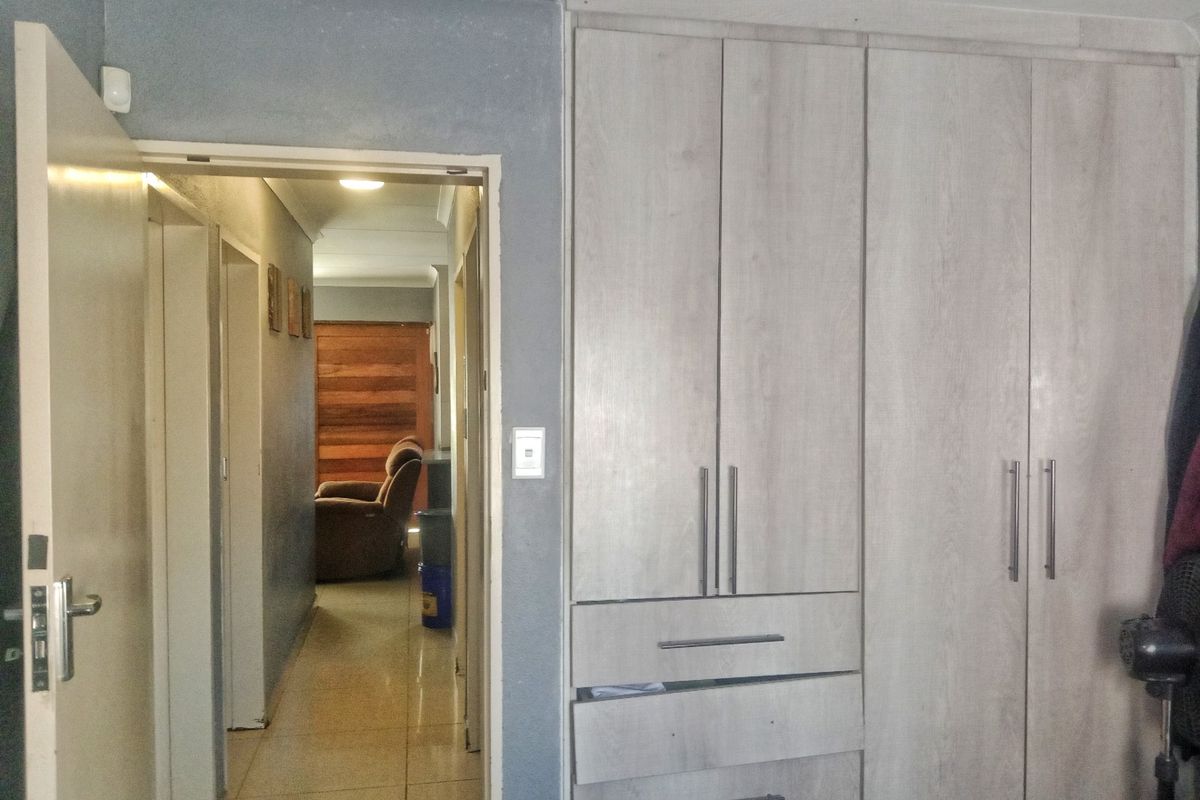 A bedroom interior featuring built-in light wood-grain cabinetry and a doorway leading into a tiled hallway.