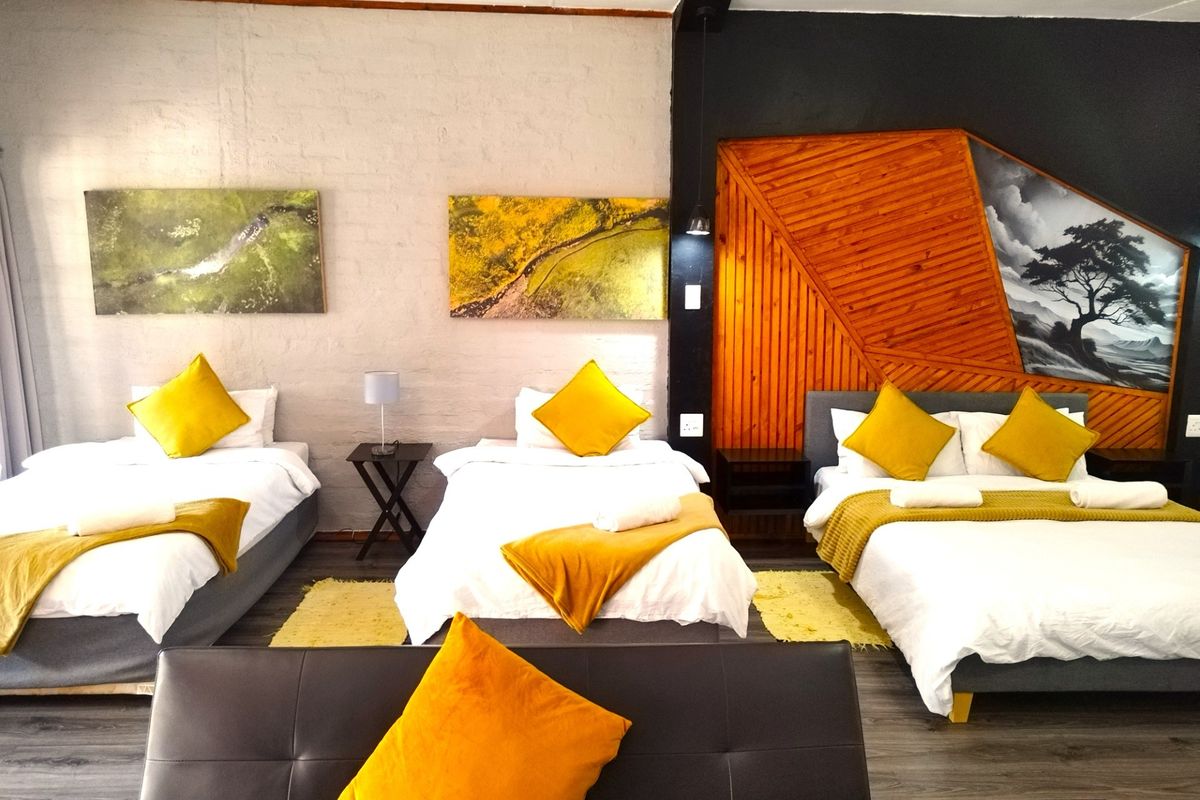 A spacious bedroom featuring multiple beds, wood-paneled accent wall, and modern grey flooring, suitable for guest house accommodation.