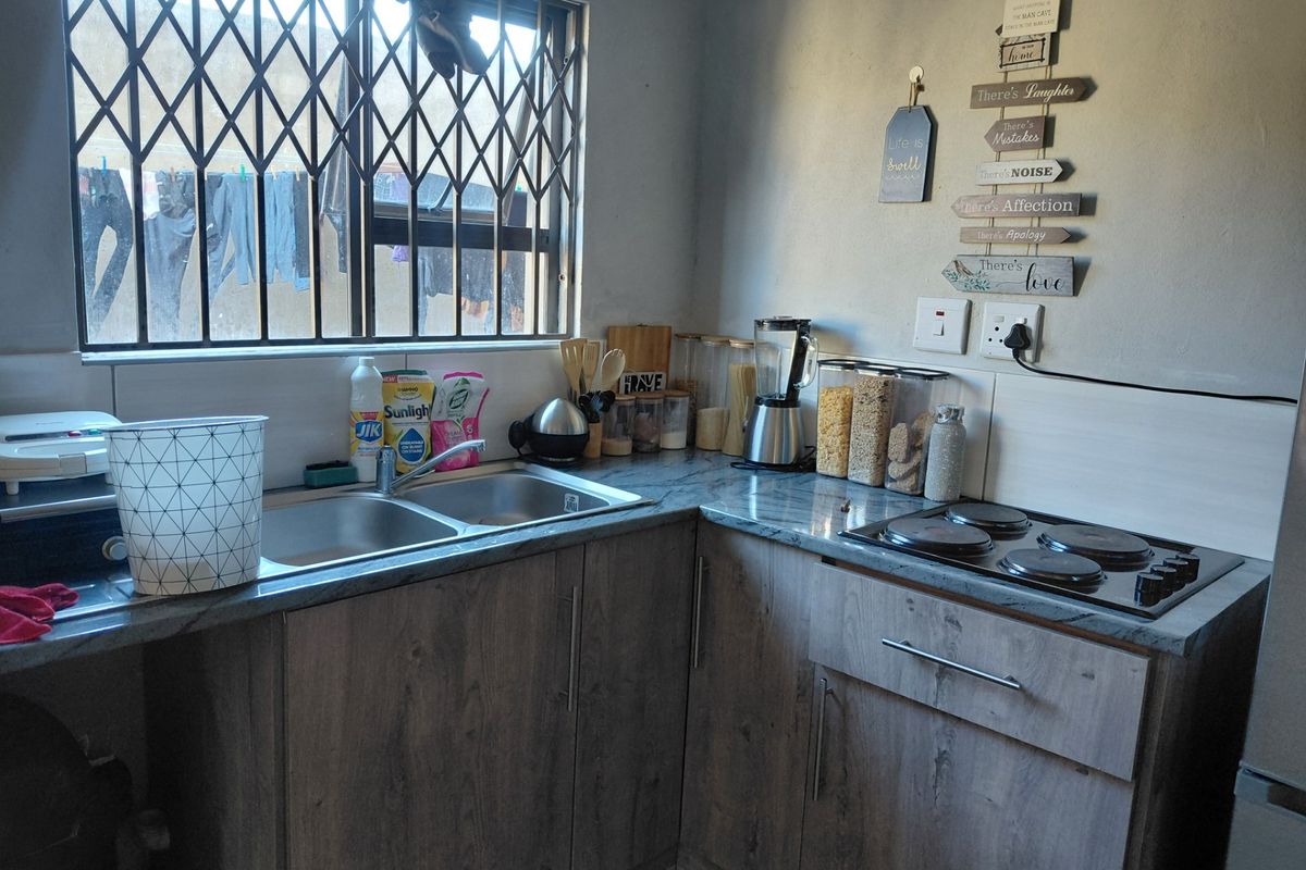 A functional kitchen featuring wood-look cabinetry, laminate countertops, a double bowl sink, and a built-in electric hob with a security gate on the window.