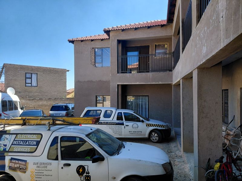 Rear view of a multi-story apartment building showing balconies, metal railings, and unfinished exterior plastering work.