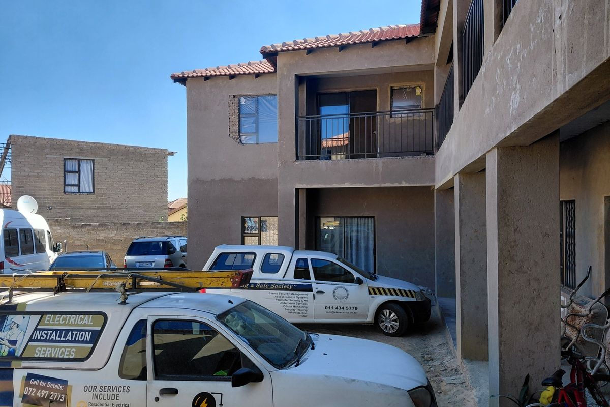 Rear view of a multi-story apartment building showing balconies, metal railings, and unfinished exterior plastering work.