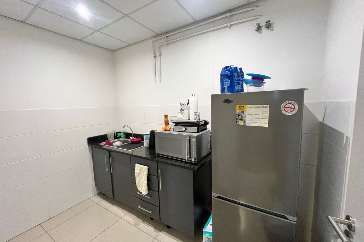 A functional kitchenette area featuring dark grey cabinetry, a granite countertop, a stainless steel sink, and tiled flooring within an industrial office space.