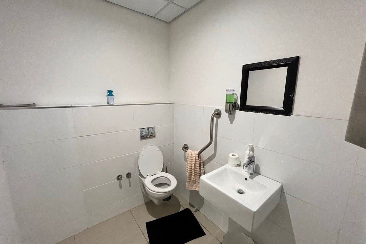 Functional industrial restroom featuring a wall-mounted toilet, pedestal sink, and accessibility grab rail with tiled walls and flooring.