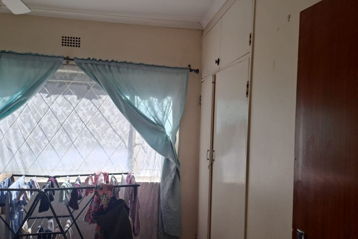 A bedroom featuring built-in cupboards and a window with security bars, offering a functional space with potential for cosmetic updates.