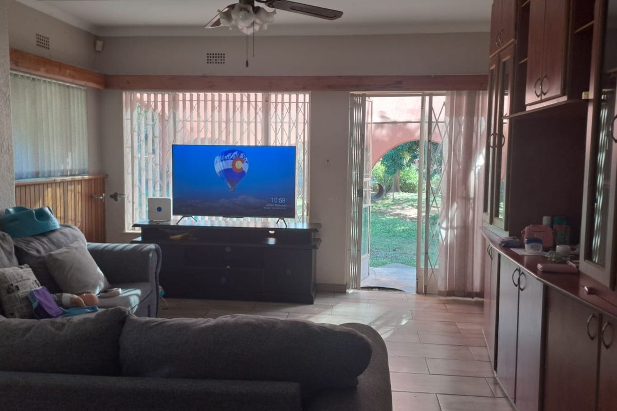 A living room featuring tiled flooring, built-in wooden cabinetry, a ceiling fan, and direct access to the garden through a security gate.