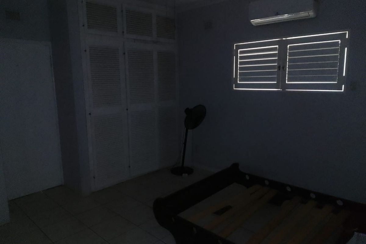 A bedroom featuring built-in cupboards, tiled flooring, and a wall-mounted air conditioning unit.