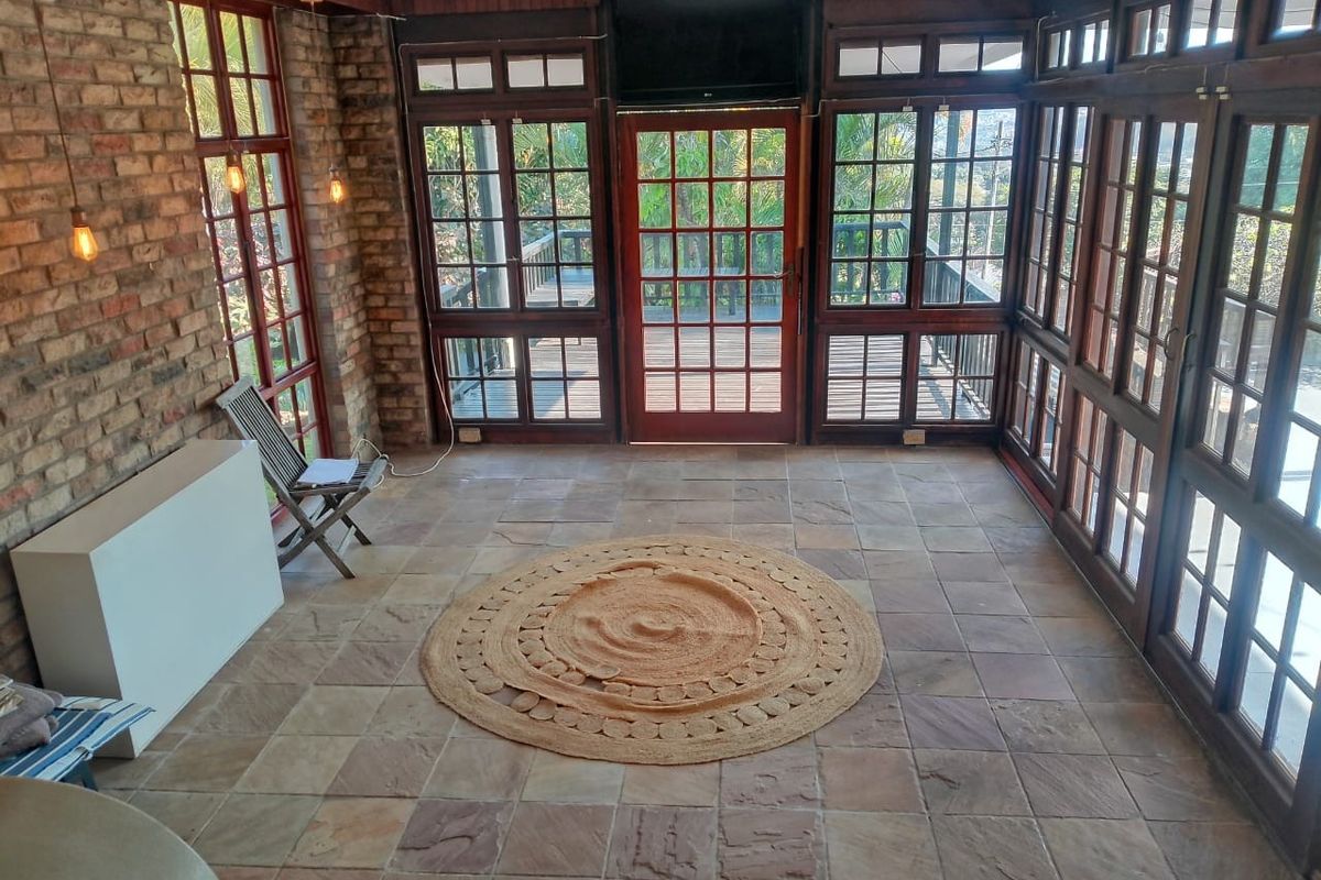 Sunroom featuring exposed brick walls, stone tile flooring, and extensive timber-framed glazing with direct access to an outdoor deck area.