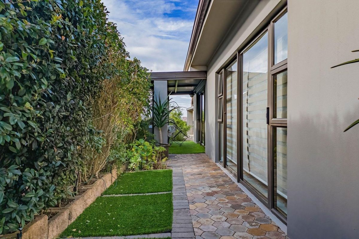 A well-maintained rear exterior featuring a paved walkway, artificial turf sections, and large sliding glass doors providing access to the home.