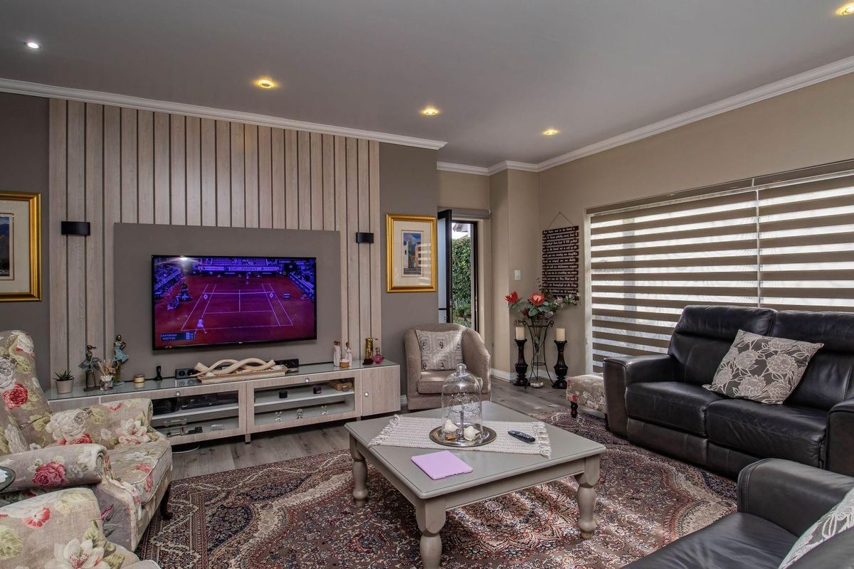 A well-maintained living room featuring a modern timber slat feature wall, recessed downlighting, and neutral laminate flooring with large windows and roller blinds.
