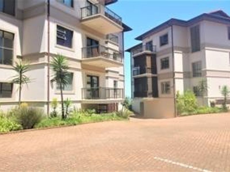 Exterior view of a modern apartment complex featuring multi-level balconies, paved driveway access, and well-maintained building facades.