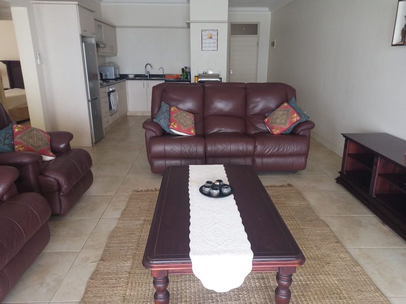 Open-plan living area featuring tiled flooring and a functional kitchen with built-in cabinetry and appliances.