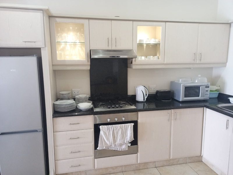 A functional kitchen featuring light wood cabinetry, granite countertops, a gas hob with extractor fan, and built-in oven with glass-fronted display cabinets.