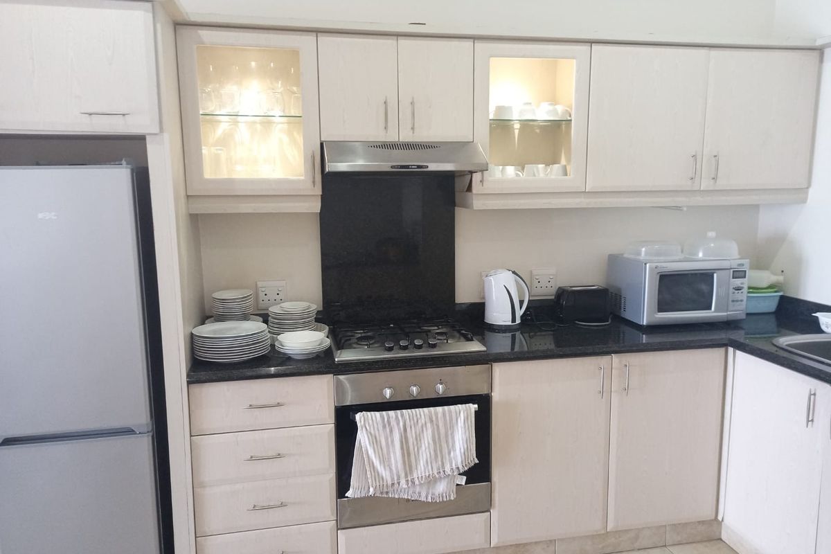 A functional kitchen featuring light wood cabinetry, granite countertops, a gas hob with extractor fan, and built-in oven with glass-fronted display cabinets.