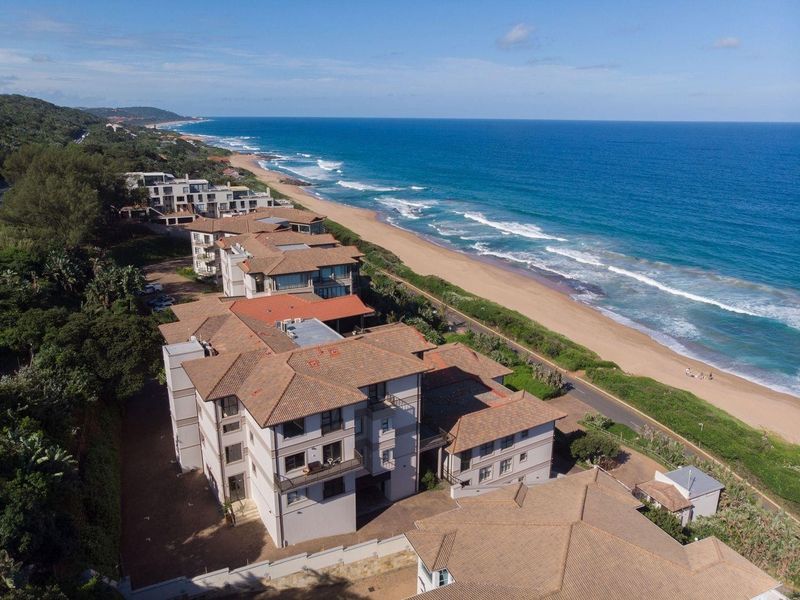 Aerial view of a coastal apartment complex featuring tiled roofs, balconies, and direct proximity to the beach and ocean.