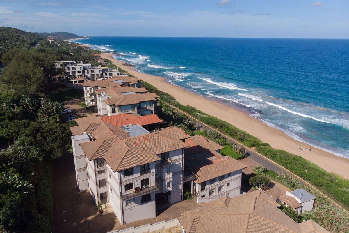 Aerial view of a coastal apartment complex featuring tiled roofs, balconies, and direct proximity to the beach and ocean.