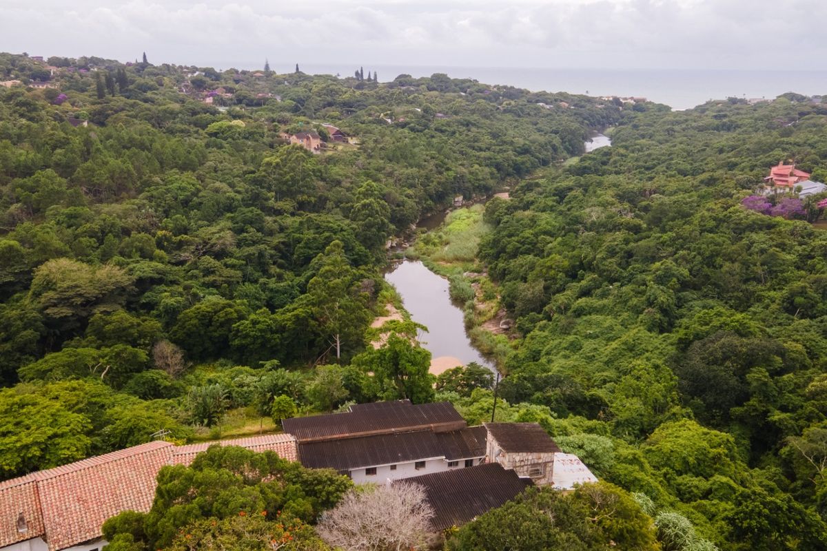 Aerial view of the property featuring a multi-pitched roof structure, surrounded by dense natural forest and a river landscape.