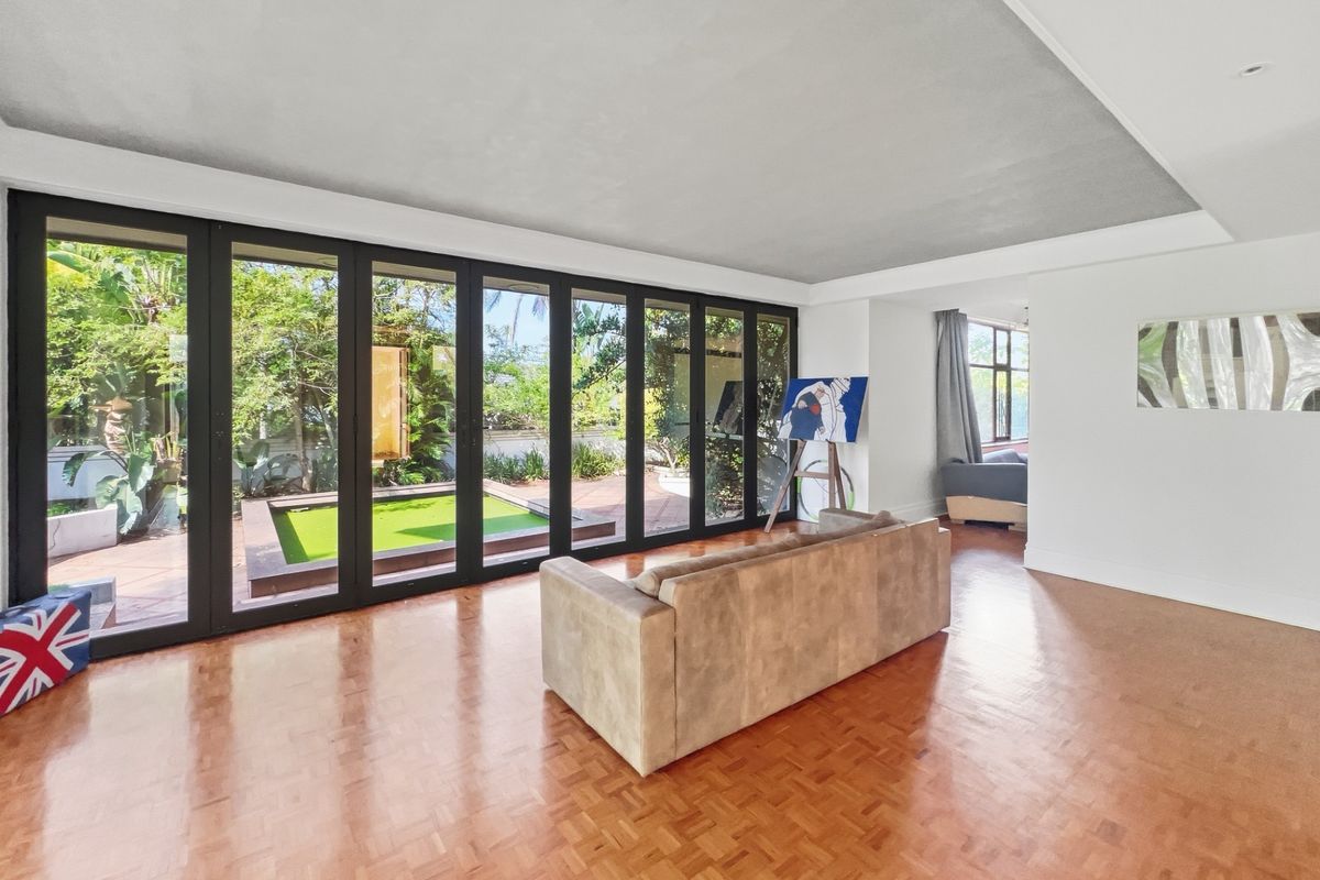 Spacious living area featuring parquet flooring and large black-framed folding glass doors that open onto a private patio and garden area.