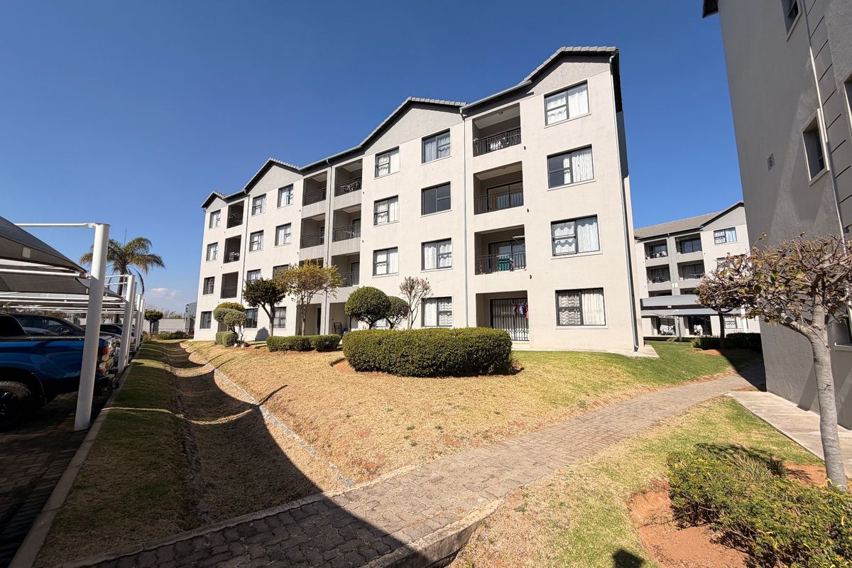 Exterior view of a multi-story apartment complex featuring paved walkways, landscaped garden areas, and covered parking bays.
