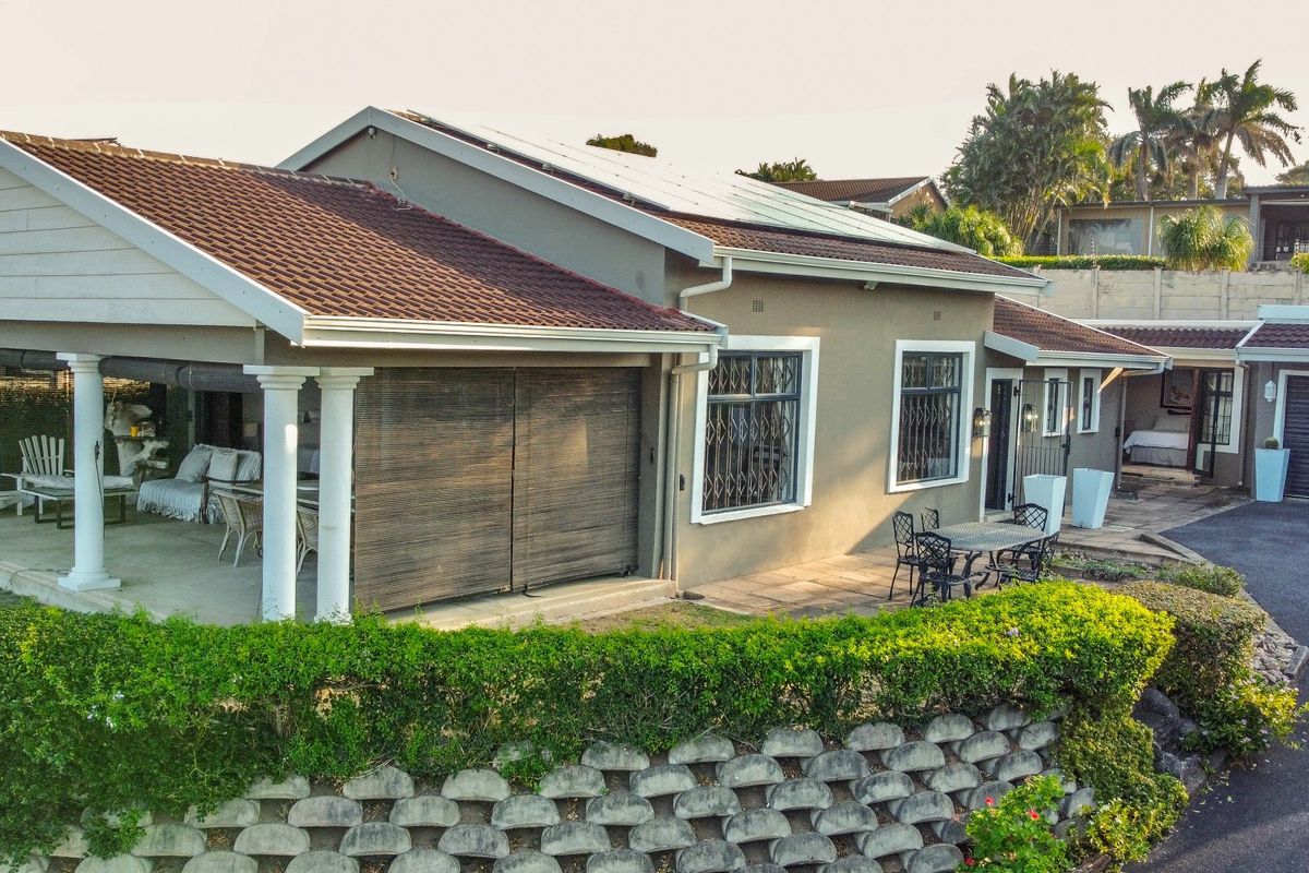 An elevated view of the property featuring a covered patio with classic columns, tiled roof, solar panels, and a paved driveway area.